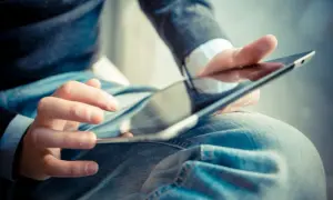 Dłonie mężczyzny w dżinsach i swetrze korzystają z tabletu. Może szuka ulgi na internet co ile lat?