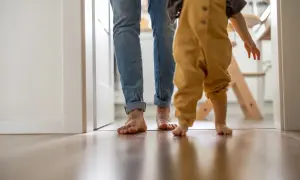 Rodzic i dziecko idą boso po drewnianej podłodze. Czy urlop wychowawczy jest płatny? To pytanie nurtuje wielu rodziców.