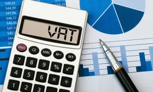 Kalkulator z napisem VAT na wyświetlaczu leży obok wykresów i długopisu. Przygotowanie do rozliczenia JPK VAT.
