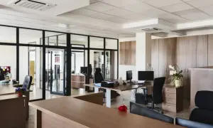 Nowoczesne biuro z przeszklonymi ścianami, biurkami i czarnymi fotelami.