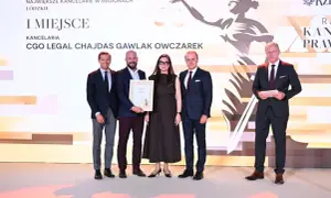 Cztery osoby w garniturach stoją na scenie, odbierając nagrodę.