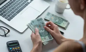 Kobieta liczy banknoty 100 zł, obok laptop, kalkulator i okulary. Czy to kwota wolna od zajęcia?