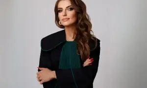 Kobieta w todze prawniczej, z rękami skrzyżowanymi na piersi, na jasnym tle.