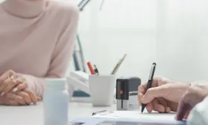 Lekarz wypisuje zwolnienie lekarskie wstecz. Pacjentka czeka, obok stoi biała buteleczka leków.