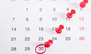 Zbliżenie na kalendarz z zaznaczonymi czerwonymi pinezkami i zakreśloną datą 30.