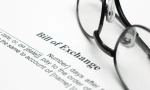 Okulary leżą na dokumencie "Bill of Exchange", czyli wekslu. Widoczne są fragmenty tekstu dotyczące daty i płatności.