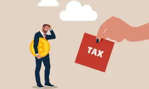 Zmartwiony mężczyzna z monetą Bitcoin w ręku, któremu wręczono kartkę z napisem TAX. Ile podatku od kryptowalut?