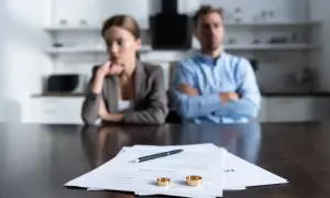 Para rozwiedzionych siedzi przy stole z dokumentami rozwodowymi i obrączkami.
