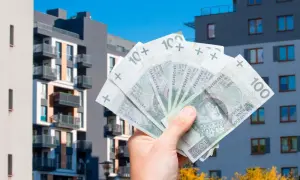 Dłoń trzyma banknoty 100 zł na tle nowoczesnych bloków mieszkalnych. To symbol ulgi mieszkaniowej i możliwości zakupu własnego M.