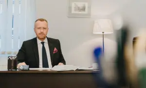 Mężczyzna w garniturze siedzi przy biurku, przed nim otwarta księga.