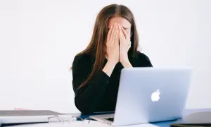 Kobieta z dłońmi na twarzy, przygnębiona przez zniesławienie w internecie.