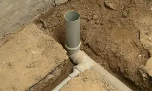 Wykonano przyłącze wody. Szare rury kanalizacyjne ułożone w wykopie, otoczone ziemią i fragmentami betonu.