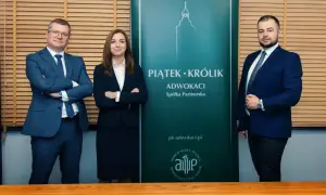 Trzy osoby w garniturach stoją przed zielonym banerem kancelarii.