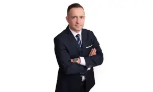 Mężczyzna w garniturze z rękami skrzyżowanymi na piersi, na białym tle.