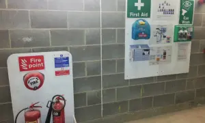 Tablica informacyjna budowy z gaśnicami, apteczką i instrukcjami bezpieczeństwa.