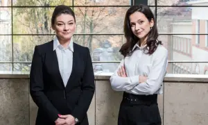 Dwie kobiety w strojach biznesowych stoją przed oknem z widokiem na miasto.