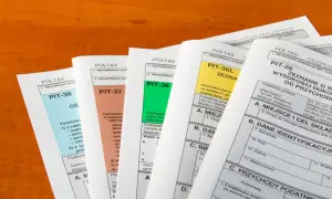 Stos dokumentów PIT, w tym PIT-36L, PIT-37, PIT-38, PIT-36 i PIT-28, leżących na drewnianym blacie.