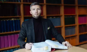 Mężczyzna w garniturze siedzi przy stole z otwartą księgą, otoczony regałami z książkami. Zastanawia się, ile bierze adwokat za reprezentowanie w sądzie.