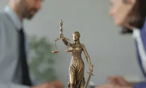 Figurka Temidy z wagą i mieczem na tle niewyraźnych postaci prawników.