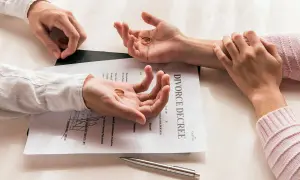 Dwie dłonie trzymają obrączki, leżące na dokumencie "DIVORCE DECREE". Symboliczny koniec małżeństwa, czas na rozwód.