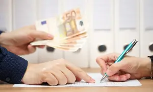 Dwie osoby przy biurku. Jedna podaje plik banknotów 50 euro, druga podpisuje dokument. To może być moment, kiedy należy się odprawa.