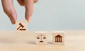 Dłoń układa kostki z symbolami prawa: młotek sędziowski, waga sprawiedliwości i budynek sądu, symbolizujące jurysdykcję.