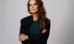 Kobieta w todze prawniczej, z rękami skrzyżowanymi na piersi, na jasnym tle.