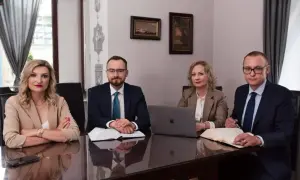 Cztery osoby w strojach biznesowych siedzą przy stole w sali konferencyjnej.