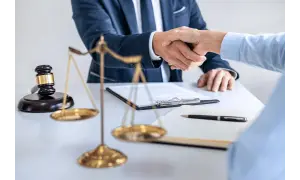 Dwóch prawników ściska sobie dłonie przy biurku, na którym leży młotek sędziowski i waga sprawiedliwości. Sprawa 157 kk zakończona sukcesem.