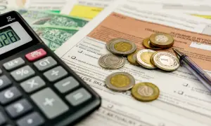 Kalkulator, monety i dokumenty podatkowe leżą na stole, czekając na rozliczenie. Kiedy zwrot podatku jest blisko, liczenie staje się prostsze.