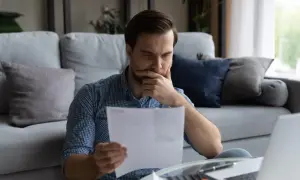 Mężczyzna zamyślony czyta dokumenty przy laptopie.