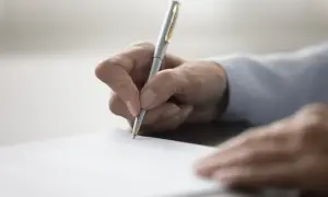Dłoń pisze długopisem na papierze, przygotowując dokument. Dowiedz się, jak napisać testament.