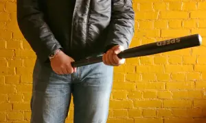 Mężczyzna w czarnej kurtce i jeansach trzyma kij baseballowy z napisem "SPEED". Groźny rozbój wisi w powietrzu.