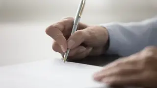 Dłoń pisze długopisem na papierze, przygotowując dokument. Dowiedz się, jak napisać testament.