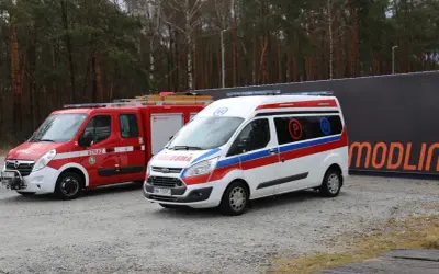 Strażackie i ratownicze pojazdy, gotowe do akcji. W tle las i napis "MODLIN". Idealne do kurs na pojazdy uprzywilejowane.