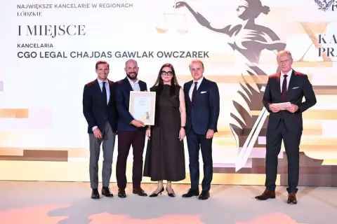 Cztery osoby w garniturach stoją na scenie, odbierając nagrodę.