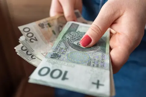 Dłonie trzymają stos polskich banknotów 100 i 200 zł. Czas na przelew podatkowy.