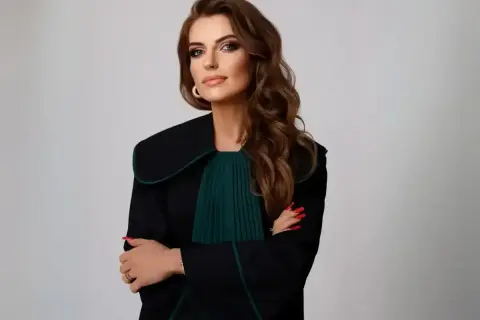 Kobieta w todze prawniczej, z rękami skrzyżowanymi na piersi, na jasnym tle.
