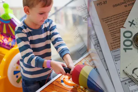 Chłopiec bawi się zabawką, a obok leżą dokumenty PIT i pieniądze. To symbol ulgi na dziecko, która pozwala na odliczenia podatkowe.