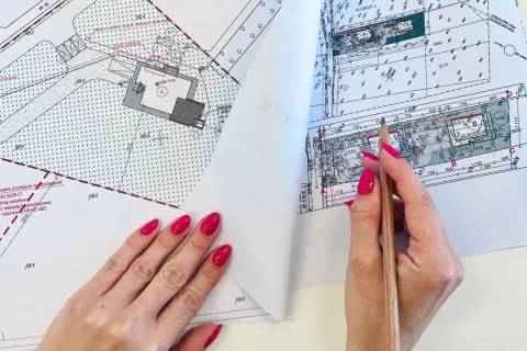 Ręka z różowymi paznokciami wskazuje ołówek na mapie do celów projektowych, gdzie widoczne są plany budowy przyłącza wodociągowego.