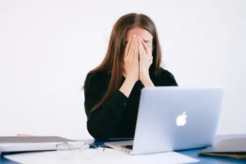 Kobieta z dłońmi na twarzy, przygnębiona przez zniesławienie w internecie.