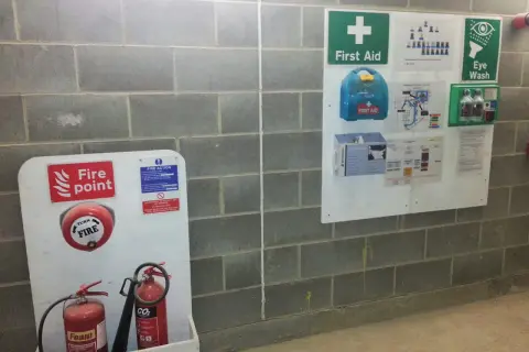 Tablica informacyjna budowy z gaśnicami, apteczką i instrukcjami bezpieczeństwa.