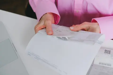 Dłonie trzymają dokumenty, na jednym z nich widnieje kwota 150,00 zł. To może być faktura uproszczona.