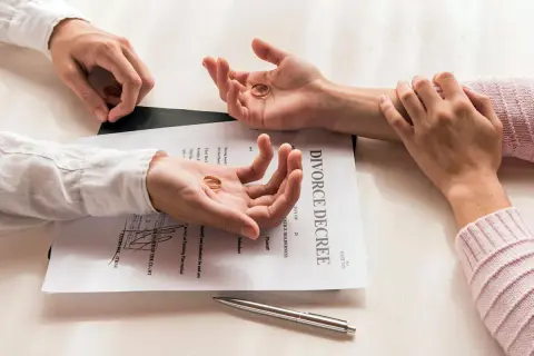 Dwie dłonie trzymają obrączki, leżące na dokumencie "DIVORCE DECREE". Symboliczny koniec małżeństwa, czas na rozwód.