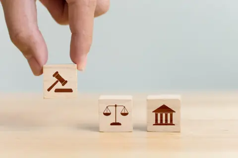 Dłoń układa kostki z symbolami prawa: młotek sędziowski, waga sprawiedliwości i budynek sądu, symbolizujące jurysdykcję.