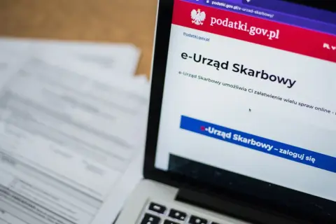 Laptop z otwartą stroną e-Urzędu Skarbowego. Obok leżą dokumenty, co sugeruje identyfikację zobowiązania podatkowego.