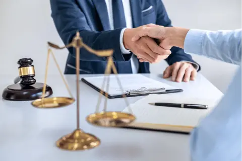 Dwóch prawników ściska sobie dłonie przy biurku, na którym leży młotek sędziowski i waga sprawiedliwości. Sprawa 157 kk zakończona sukcesem.