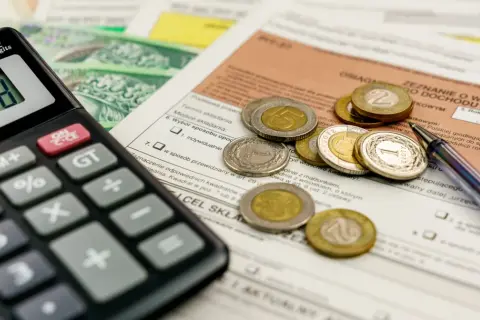 Kalkulator, monety i dokumenty podatkowe leżą na stole, czekając na rozliczenie. Kiedy zwrot podatku jest blisko, liczenie staje się prostsze.