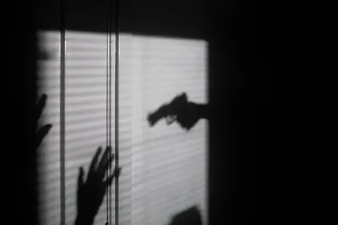 Cień dłoni z pistoletem grozi dwóm dłoniom, które próbują się zasłonić. To scena jak z filmu o świadku koronnym.