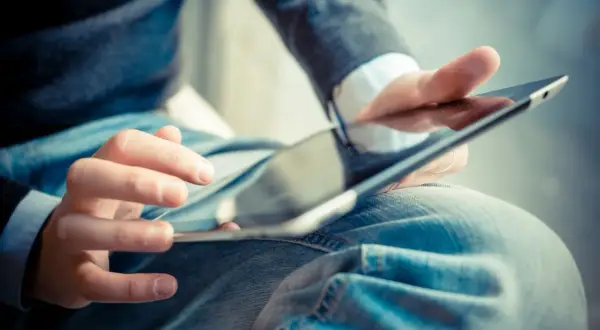 Dłonie mężczyzny w dżinsach i swetrze korzystają z tabletu. Może szuka ulgi na internet co ile lat?